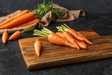 Wooden board with fresh carrots on dark background