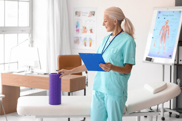 Obraz premium Mature physiotherapist with clipboard and foam roller in rehabilitation center