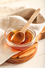 Wooden board with bowl of maple syrup and spoon on table, closeup