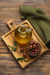 Board with decanter of fresh oil and olives on wooden background