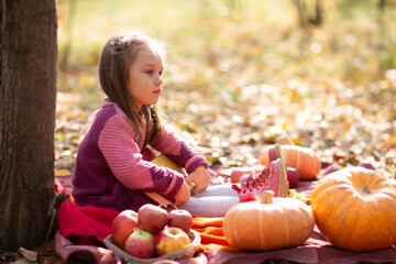 Cute little girl in autumn park with orange color leaves and yellow pumpkin