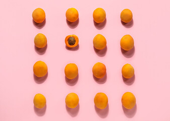Half of apricot among whole ones on pink background