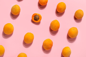 Half of apricot among whole ones on pink background
