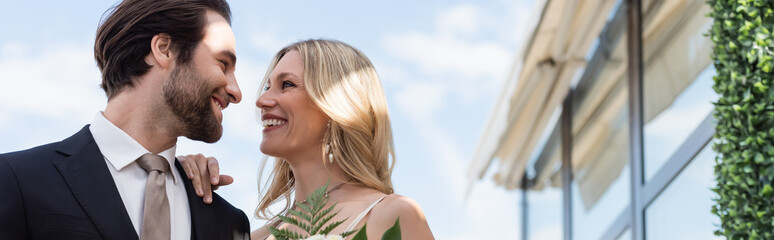 Smiling blonde bride hugging groom in suit on terrace, banner.