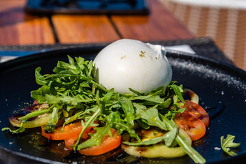 Fresh green salad made with mozzarella cheese, tomatoes, arugula and olive oil on black stone plate. Healthy food and diet concept. Side view