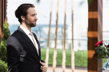 Side view of groom in elegant suit standing on terrace.