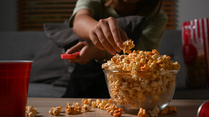 Cropped view of young woman eating popcorn and watching movie night at home