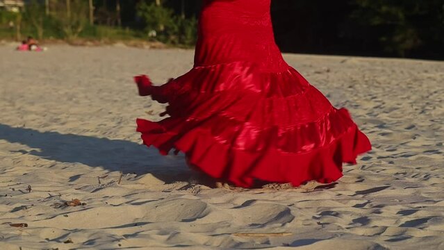 Woman in red flamenco dress dancing and spinning on beach at sunset. Gimbal, low POV