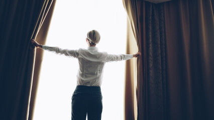 Businesswoman open curtains in hotel room at the morning and looking into window