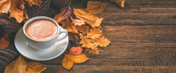 Cappuccino and autumn foliage on a wooden background. Cozy autumn composition. Side view, copy space
