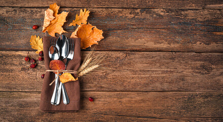 Autumn background with napkin, cutlery and autumn leaves on a wooden background with space to copy....
