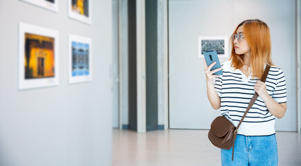 Visitor woman standing takes picture art gallery collection in front framed paintings pictures with...