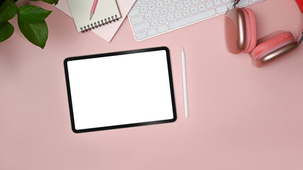 Flat lay digital tablet with empty display, notebook, headphone and houseplant on pink background