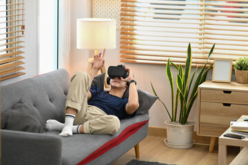 Relaxed man lying on couch and watching movie or play video game via virtual reality headset