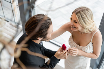 Overhead view of man holding box with proposal ring near smiling girlfriend in restaurant.