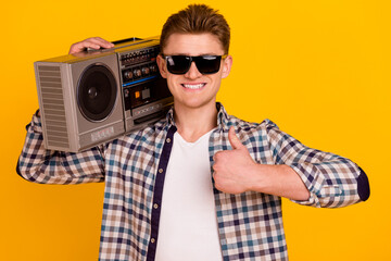 Photo of young man hold boombox show thumb-up perfect ideal sound isolated over yellow color background