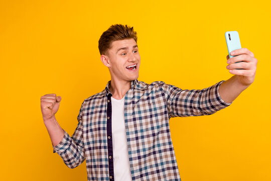Photo of young cheerful guy record video fist shand celebrate luck hooray isolated over yellow color background