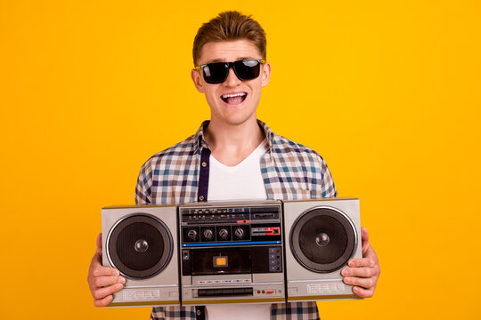 Photo of young cheerful guy hold boombox eyewear party radio sound isolated over yellow color background