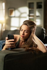 Happy young woman using the phone at home. Excited woman enjoying in the living room..