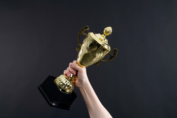 Human hand holding golden trophy cup on black background