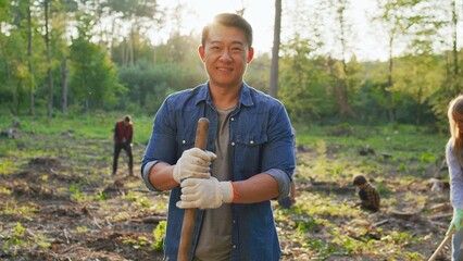 Portrait of male asian eco activist wearing gloves standing with a shovel and looking at the camera...