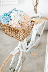 Vintage white bicycle with flowers in a basket against a white wall. Selective focus