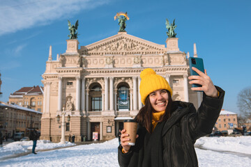 woman traveler drinking coffee to go taking selfie in front of opera building