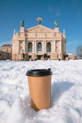 disposable coffee cup in snow lviv city opera building on background