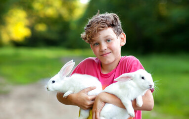 a happy pink-cheeked boy with two white rabbits in his hands