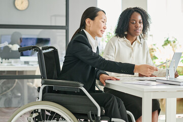 Multiethnic business colleagues using laptop while working with documents at table at office