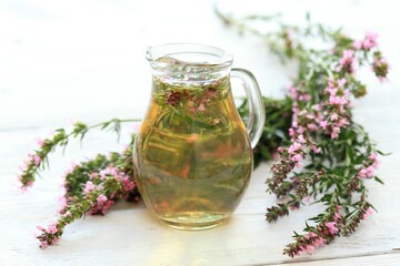Fototapeta premium Herbal tea in glass with fresh flowers of hyssopus, lat. Hyssopus officinalis. Homemade tea from hyssopus and hot water in a jug on white wooden table.