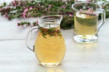 Herbal tea in glass with fresh flowers of hyssopus, lat. Hyssopus officinalis. Homemade tea from hyssopus and hot water in a jug and glass on white wooden table.