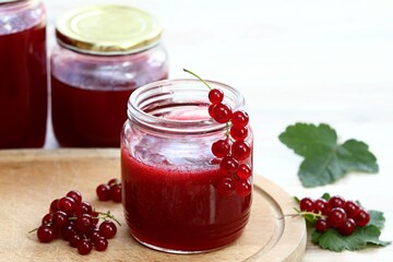 Homemade preserved red currant jam in jars. Red currants and preserved jars on white wooden table.