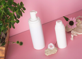 White bottle with a cosmetic products for face and body skin care with extracts of flowers and plants with reusable cotton sponges for the face. Set of cosmetic bottles on a pink background. Natural o
