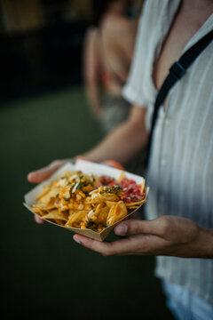 Close-up View Of The Hands Of A Festival Goer With A Serving Of Potatoes Bought From A Food Truck