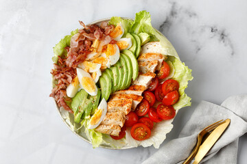 Cobb salad with avocado, tomato, grilled chicken, eggs, bacon on marble white background. Keto diet.