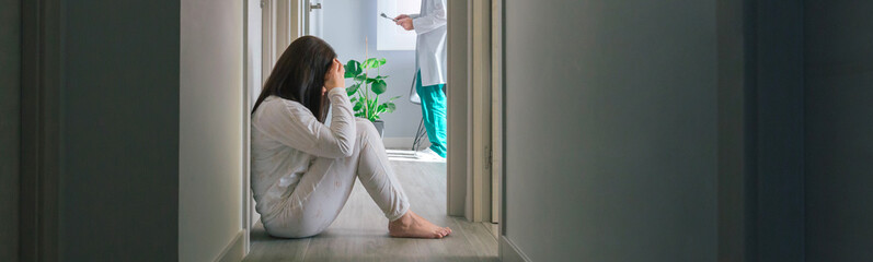 Female patient in pajamas sitting on the floor in the corridor of a mental health center with a...