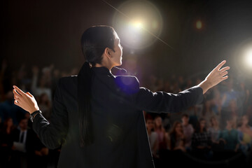 Motivational speaker with headset performing on stage, back view