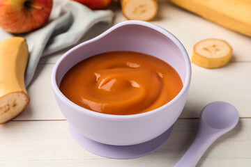 Healthy baby food in bowl and fresh fruits on white wooden table, closeup