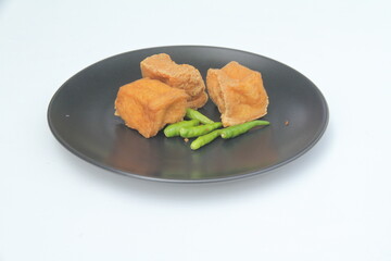 Square fried tofu with green chili on black round plate on white background
