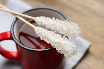 Sticks with sugar crystals and cup of tea on table, closeup