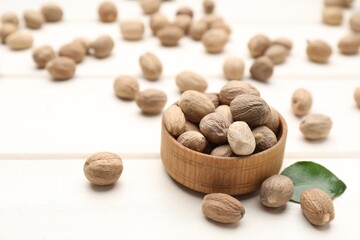 Scattered nutmeg seeds and bowl on white wooden table, closeup. Space for text