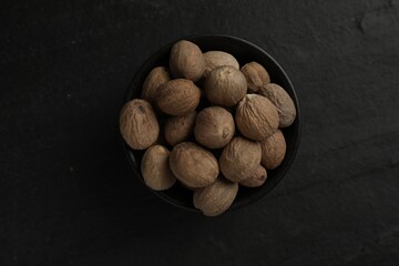 Nutmeg seeds in bowl on black table, top view