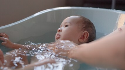 Cute baby having bath. Mother holds and bathes baby