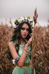 The forest fairy with long dark hair and a wreath of flowers in a long turquoise dress near...