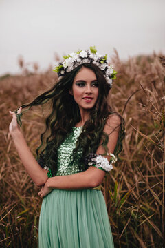 The Forest Fairy With Long Dark Hair And A Wreath Of Flowers In A Long Turquoise Dress Near Reeds.The Forest Nymph. Halloween Costume.