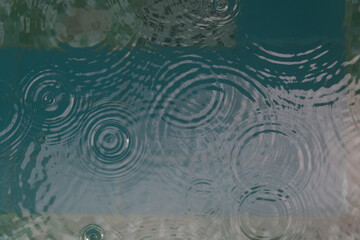 background of rain drops falling in tropical swimming pool creating circles and ripples