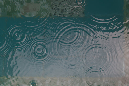 background of rain drops falling in tropical swimming pool creating circles and ripples