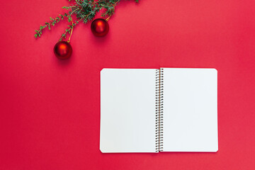 Open blank spiral notebook near Christmas tree branch with decorations on trendy red background....