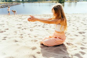 Fototapeta na wymiar Teenager thoughtful girl play with sand sitting on lake beach.